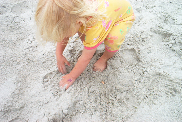A little girl burried her feet in the sand